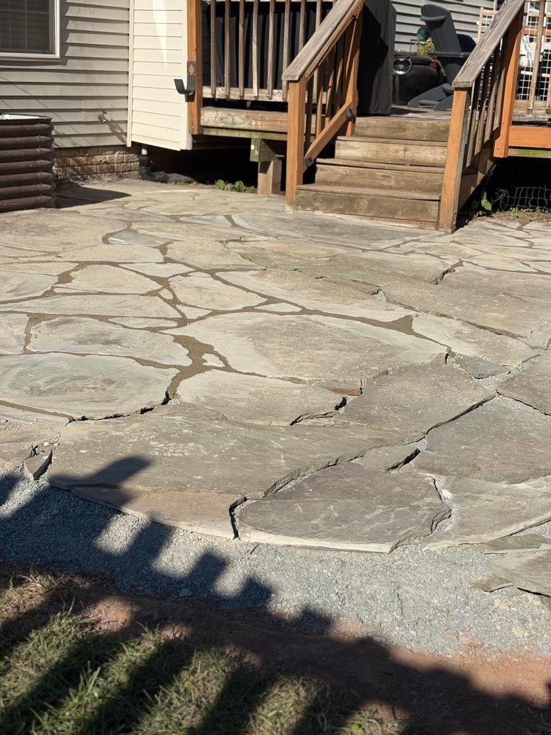 Cracked stone patio beside wooden house steps and railing in bright sunlight