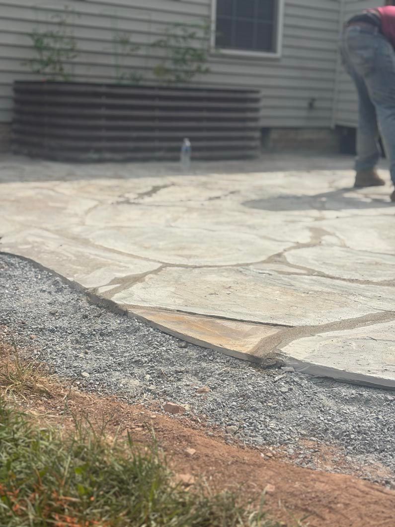 Backyard patio with stone pavers, grass edge, and a person standing near the house