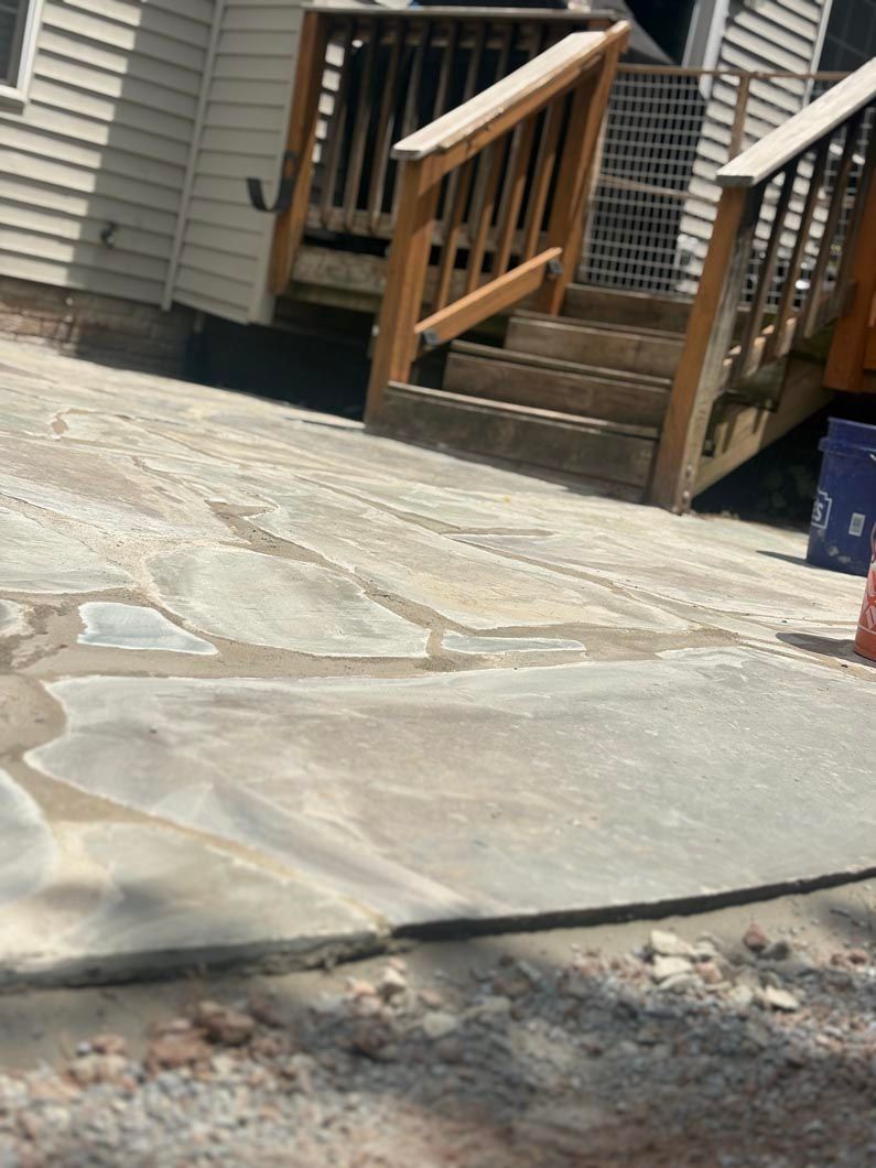 Stone patio in front of a wooden deck and house siding, with a small set of steps.