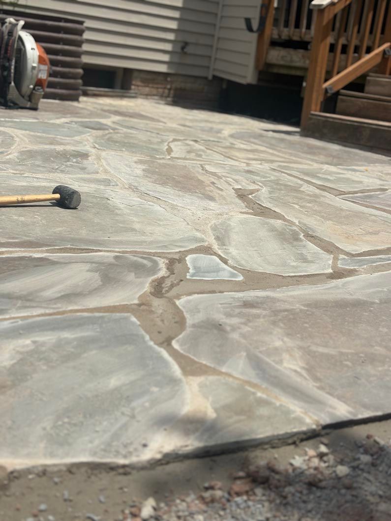 Stone patio with a hose nozzle on the left and a wooden deck in the background