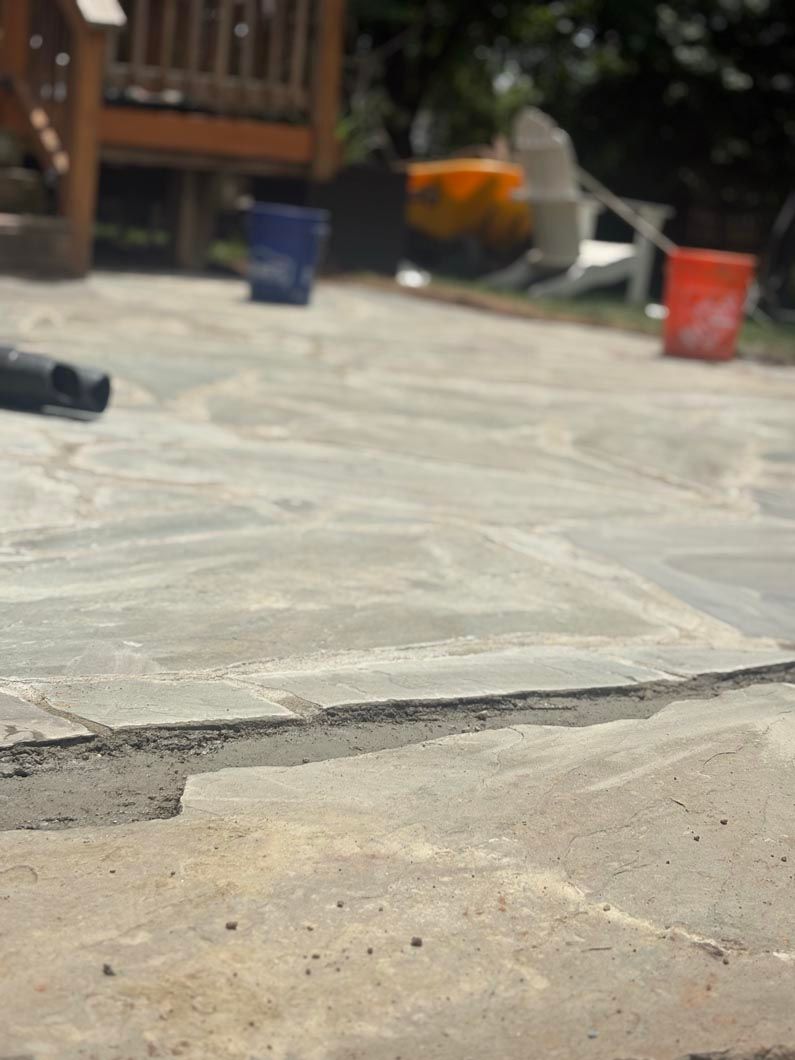 Cracked concrete patio with outdoor deck furniture and colorful buckets in the background