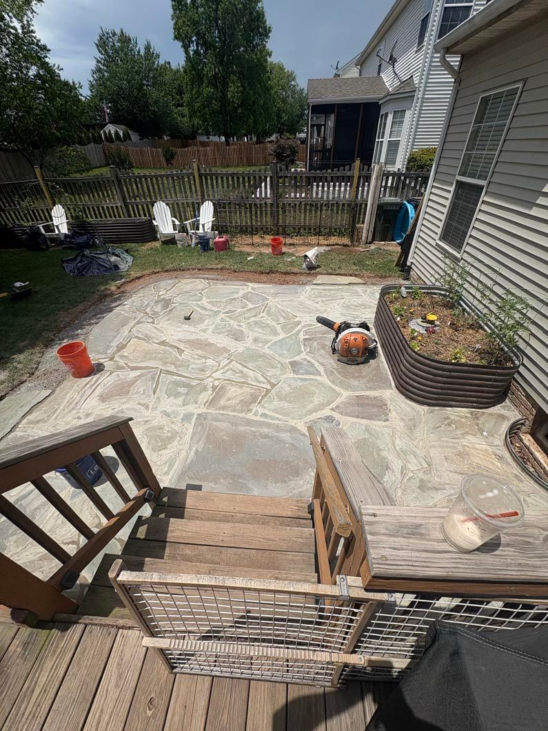 Backyard stone patio with steps, wicker chairs, potted plants, and a fenced garden beyond