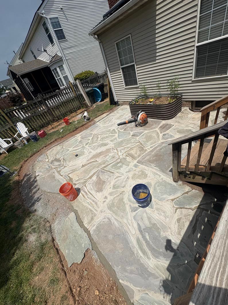 Backyard patio with plastic sheeting, planters, and a small wooden deck beside a house