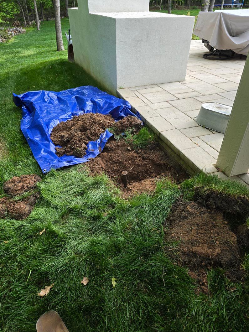 Blue tarp covering a dug-up patch of grass beside a white structure in a yard