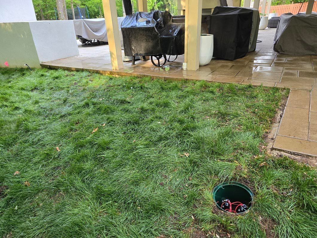 Rainy backyard patio with wet grass, a small round hole, and patio furniture under a covered area
