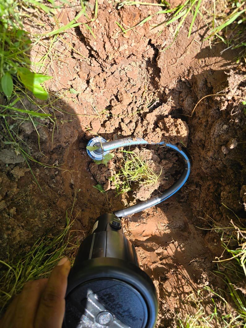 Blue cable in a dirt hole beside a small pipe or tool, viewed from above.