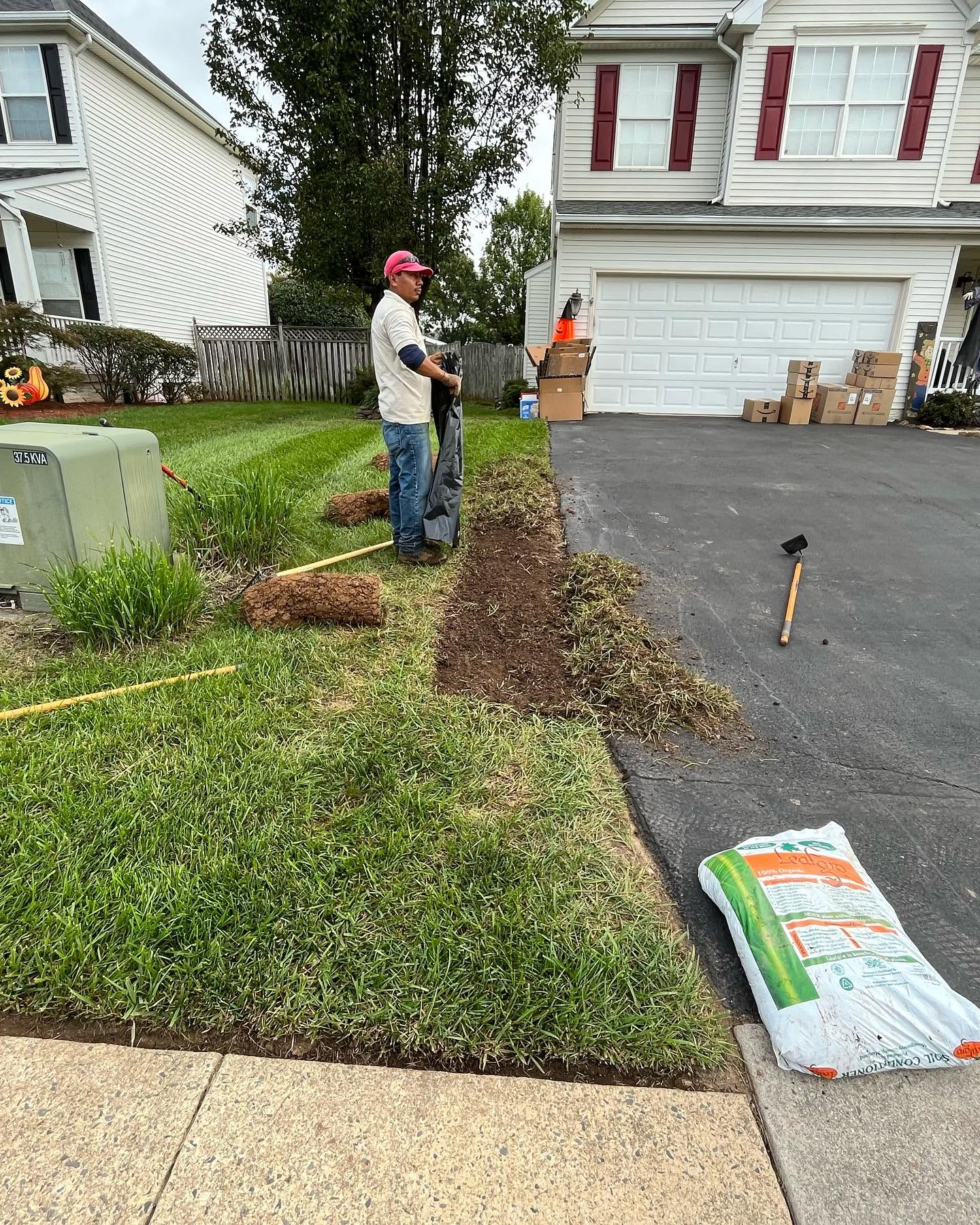 Two workers spread mulch and clear debris along a suburban front yard driveway.