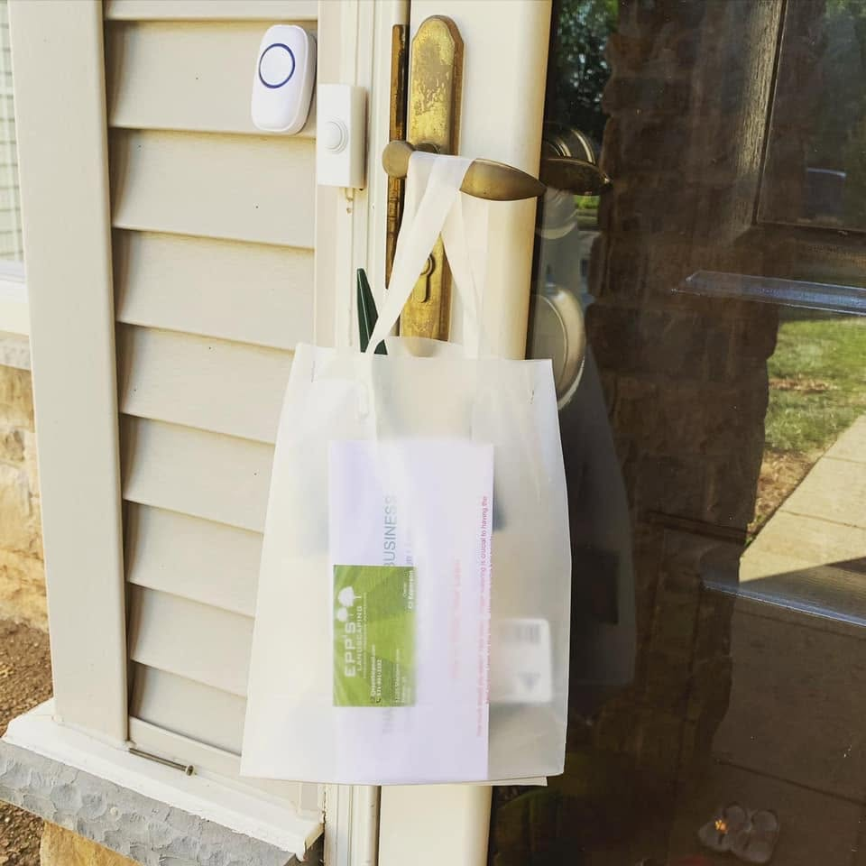 White plastic bag hanging on a front porch doorknob beside a doorbell and house siding.
