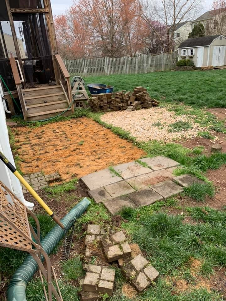 Backyard with a deck, brick and paver walkway, gravel patch, and stacked stones by a house