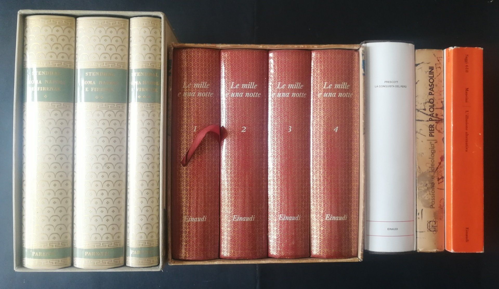 A row of assorted hardcover books in beige, red, white, and orange spines on a shelf