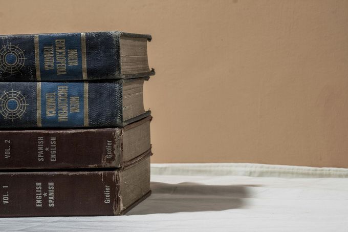 Stack of old hardcover books on a white table against a beige wall.