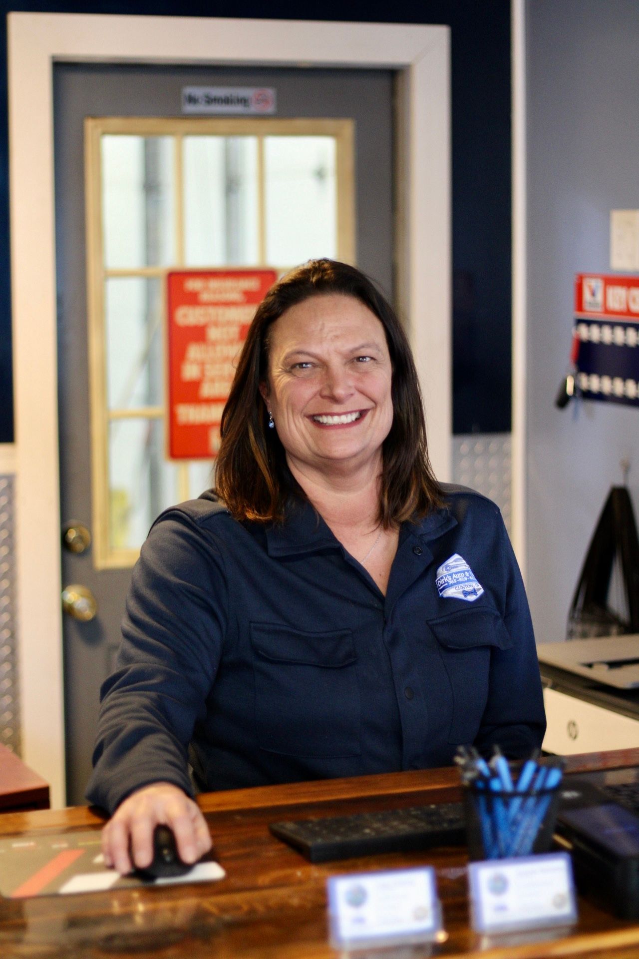 Smiling receptionist behind a desk in an office lobby, holding a computer mouse.