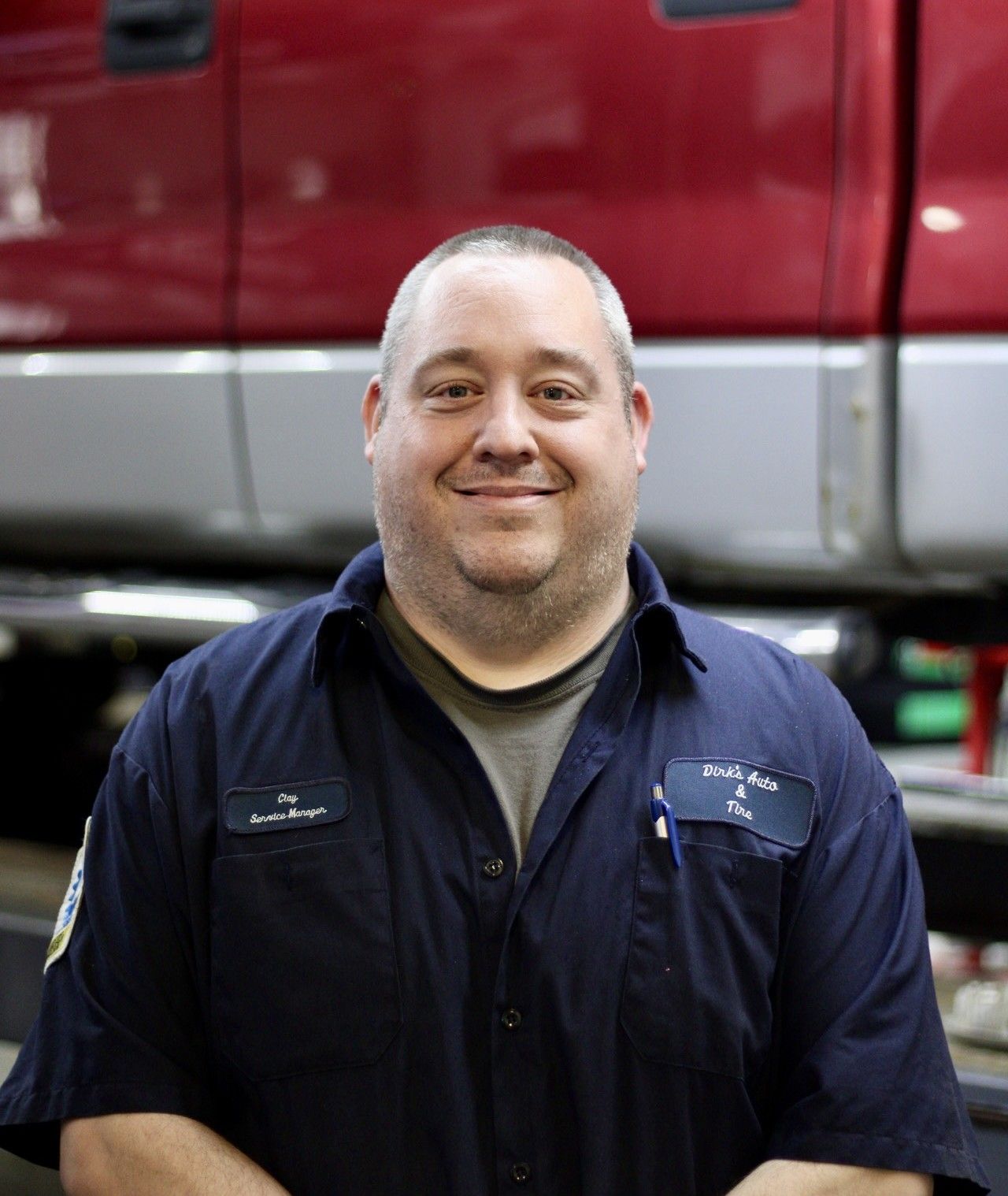 Smiling person in navy work shirt standing in front of a red vehicle