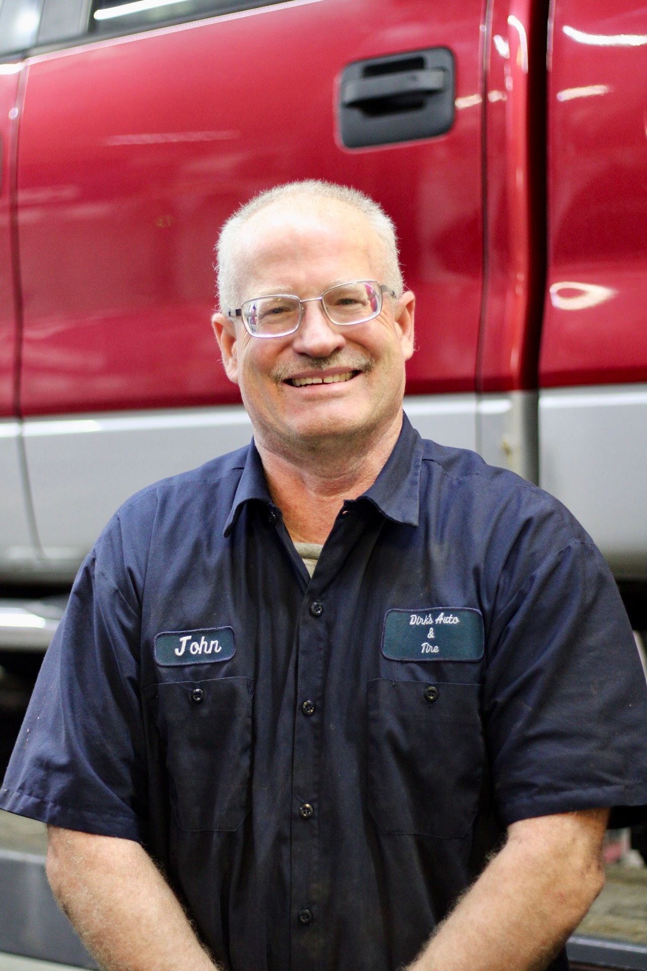Smiling mechanic in a dark blue shirt standing in front of a red truck
