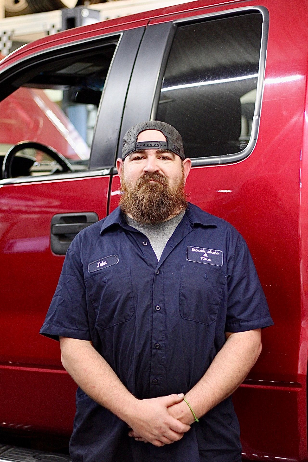 Mechanic in navy work shirt and gray cap standing in front of a red truck