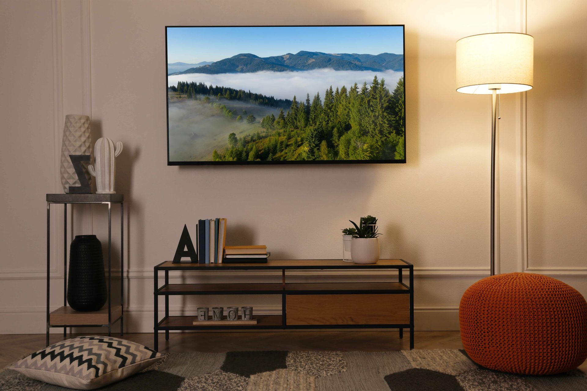 Living room with TV displaying a mountain scene, low console, floor lamp, and decorative items.