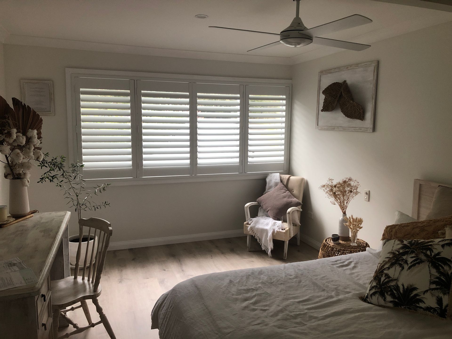 Bedroom With White Shutters, Chair, Desk, Bed, and Decor. Light Wood Flooring — My Timber Flooring Blinds & Shutters in Erina, NSW