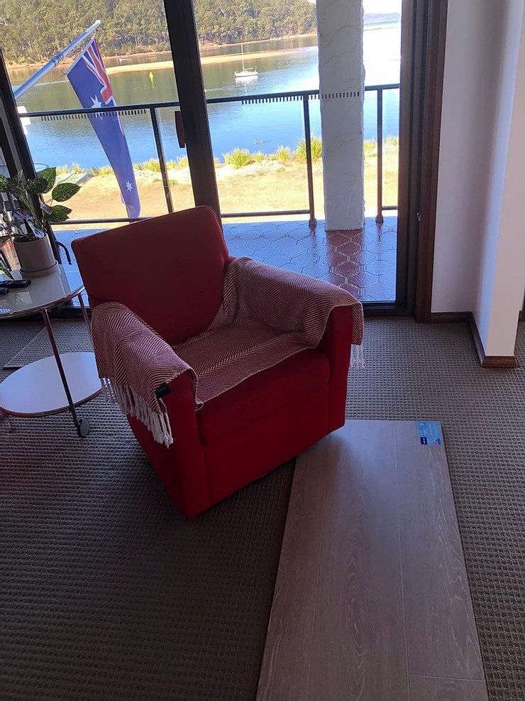 Red Armchair with A Checkered Throw, Next to A Wooden Plank, and A View of Water — My Timber Flooring Blinds & Shutters in Erina, NSW