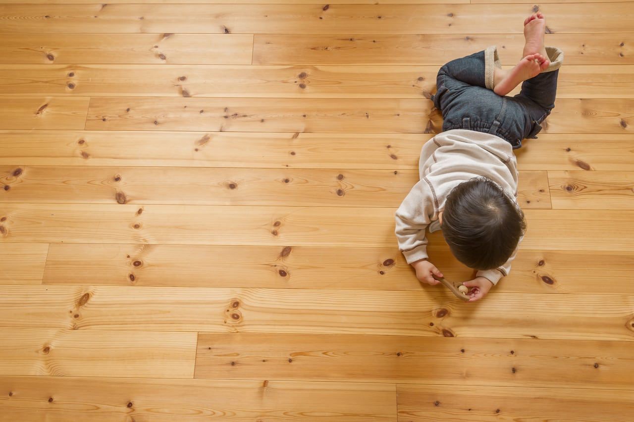 Child Lying On A Wooden Floor, Looking Down, Wearing Jeans — My Timber Flooring Blinds & Shutters in Erina, NSW