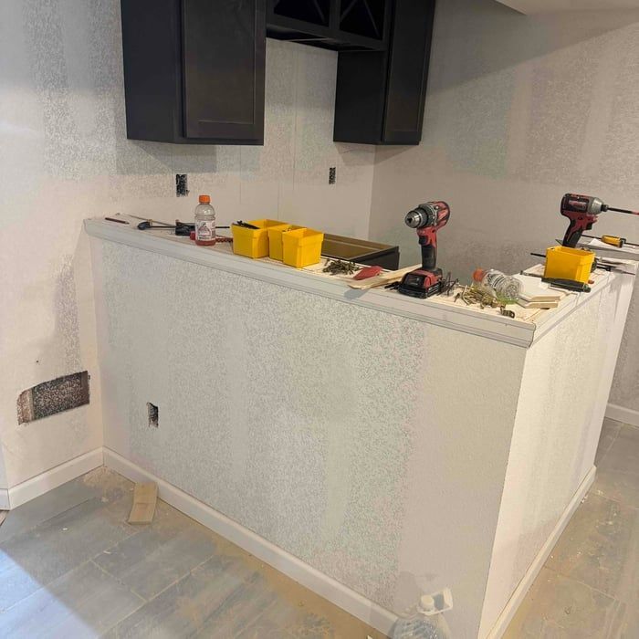 A partially constructed bar area in a room, with dark cabinets, white walls, and tools on the countertop.
