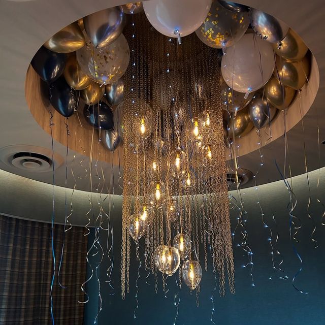Chandelier surrounded by balloons; silver, gold, and white, hanging from a circular ceiling feature.