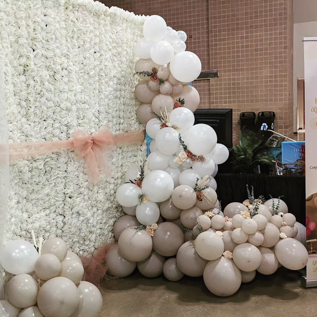 White flower wall and balloon garland display with tan, white, and blush tones.
