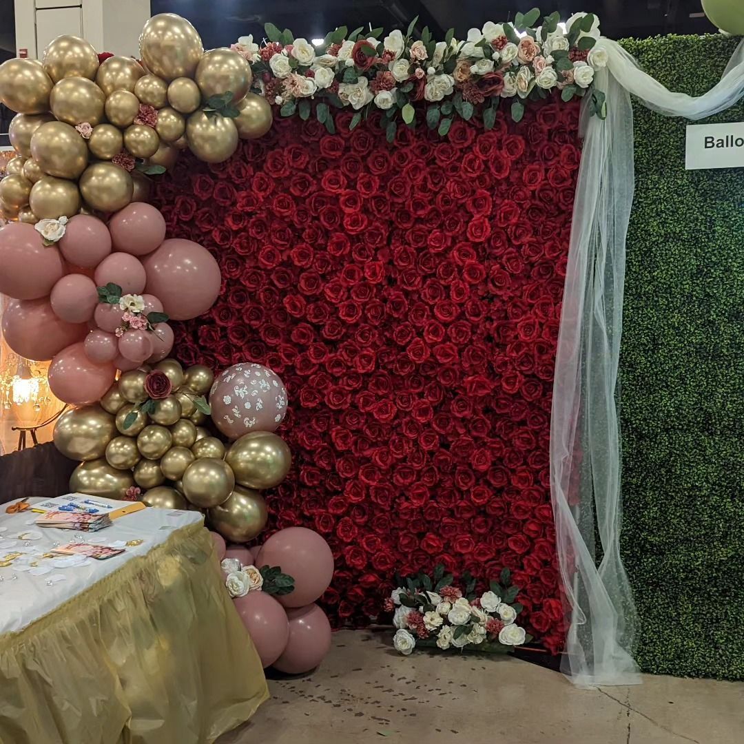 Balloon arch and floral backdrop for an event with red and gold colors.
