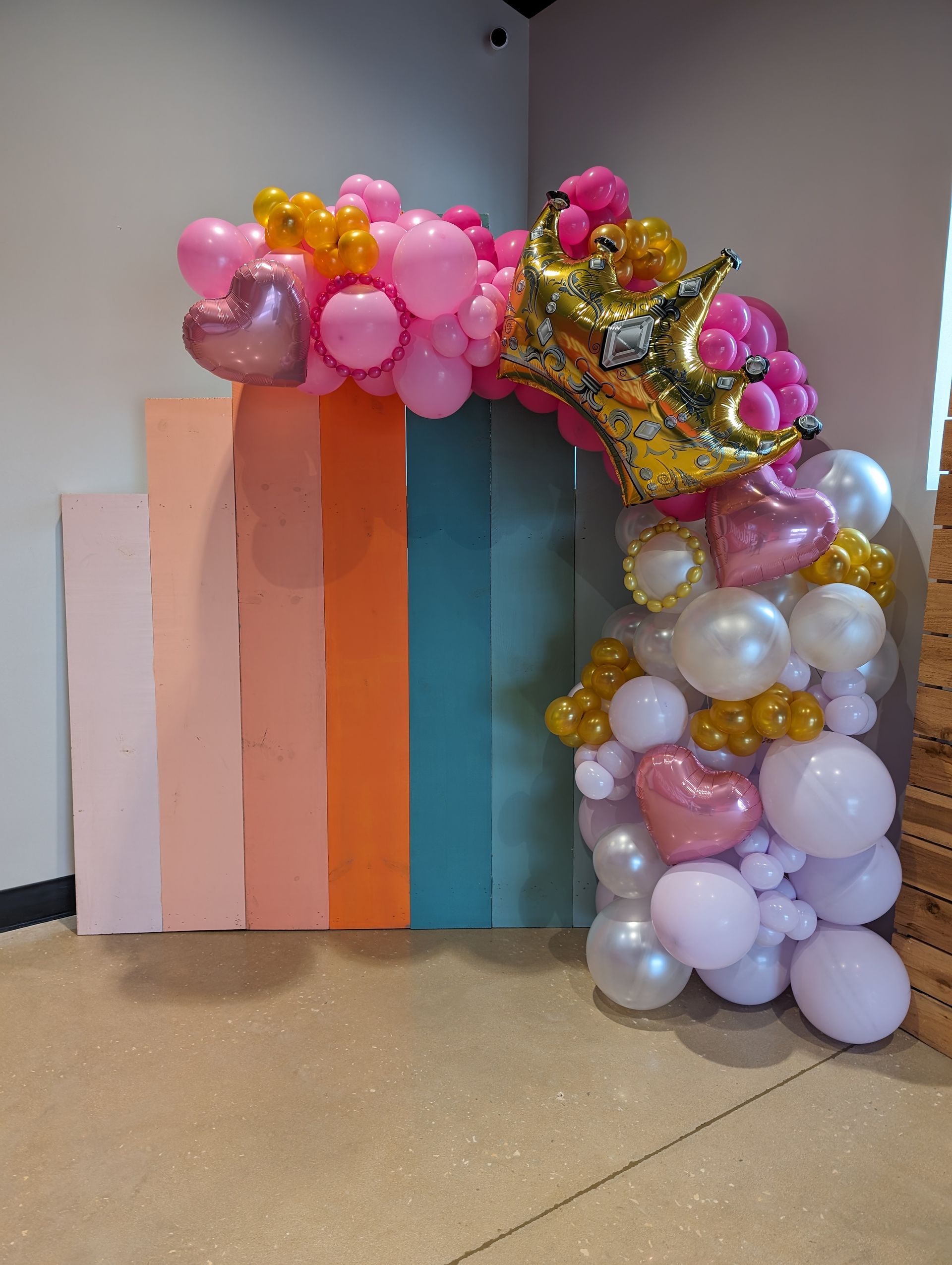 Balloon arch with crown over colorful backdrop. Pink, gold, and white balloons.
