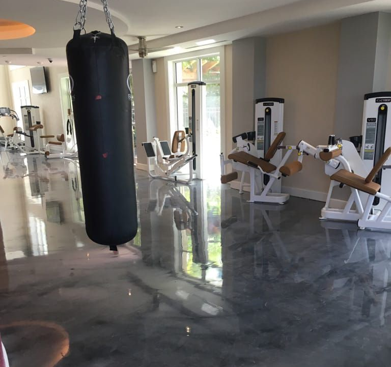 A gym room with a black punching bag hanging in the foreground and exercise machines on a polished, reflective floor.