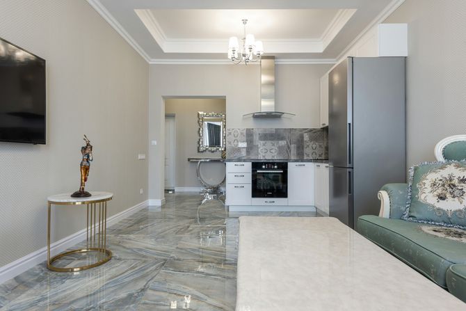 A stylish studio apartment featuring a kitchenette, marble tile floors, patterned wallpaper, and a teal patterned sofa.
