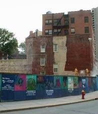 Old brick buildings behind a colorful construction fence on a city street with a red fire hydrant