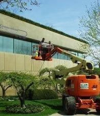 Orange utility lift boom reaching upper floor of a beige office building with a worker in the bucket