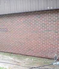 Red brick building wall with a concrete walkway and a hose on the right side.