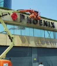 Worker on lift repairing PHOENIX sign on a glass-front building