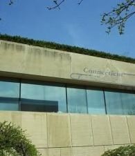 Modern building facade with reflective windows and partial sign under a blue sky