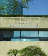 Building facade with a “Connecticut” sign, blue-tinted windows, and greenery in front.