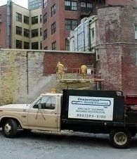 White and black utility truck parked beside a brick wall in an urban alley.