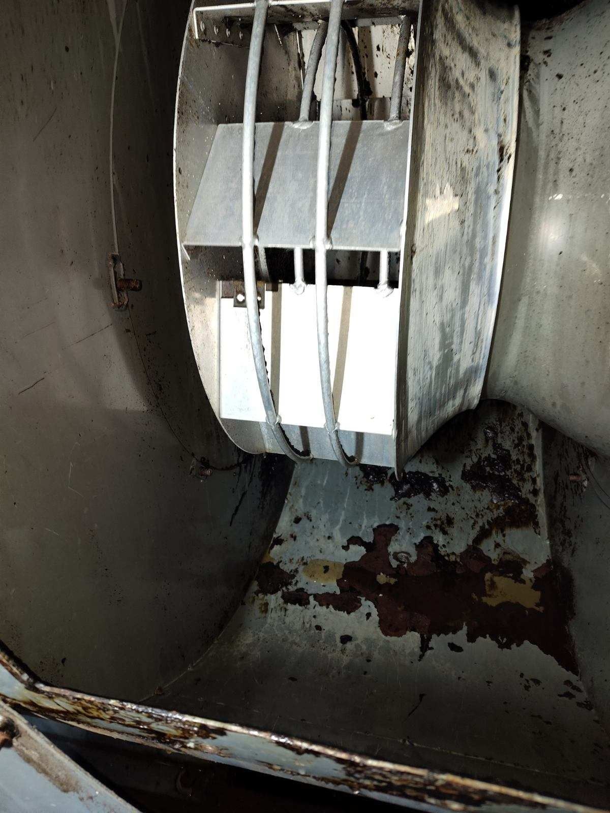 Inside a metal duct, a white fan or blower unit with visible rust and grime buildup