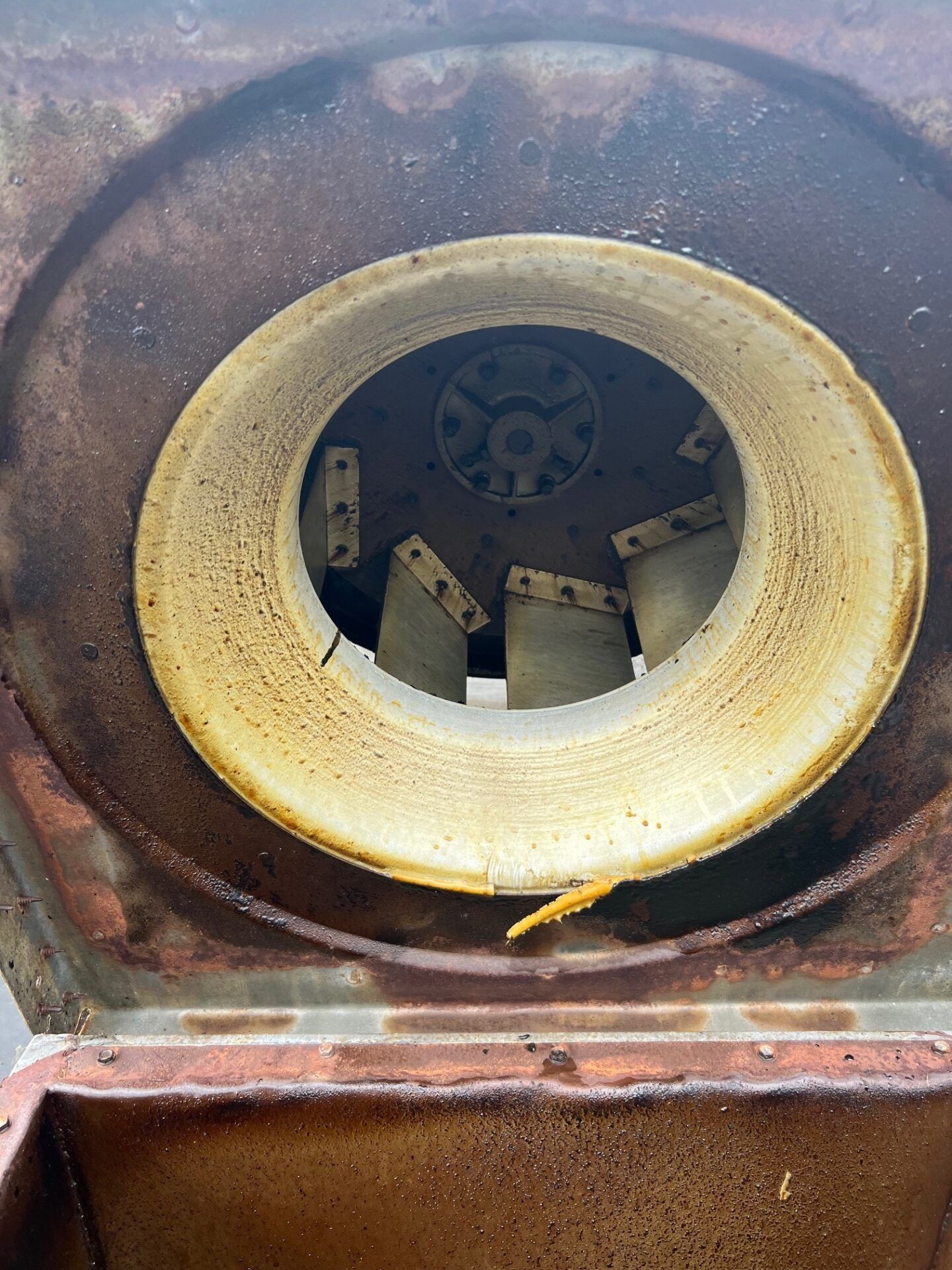 Rusty circular industrial opening with a white ring and metal blades inside.