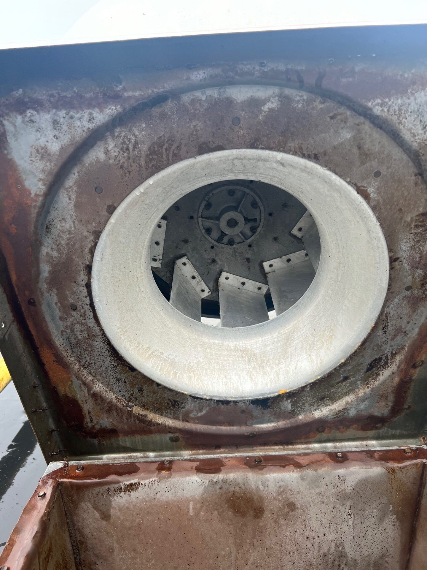 Close-up of a rusty metal hatch with a circular opening and internal fan-like blades.