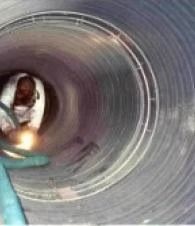 Person inside a large metal pipe, seen from the circular opening, with a teal strap in the foreground.