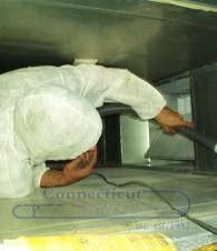 Worker in white coveralls inspecting the inside of a large metal ventilation duct.