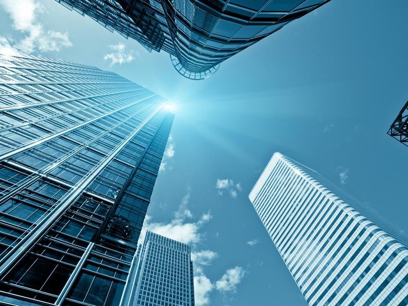 Looking up at glass skyscrapers against a bright blue sky with clouds