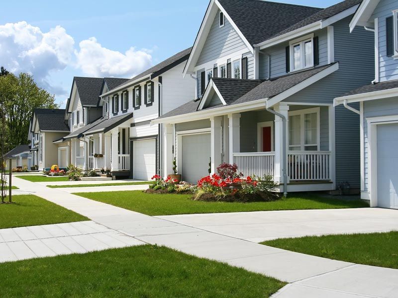 Row of gray suburban houses with white porches and green lawns along a sidewalk