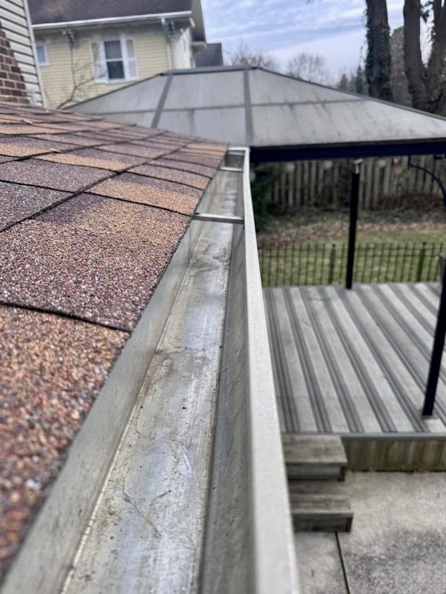 Roofline and covered patio viewed from above, with shingles, gutter, and railings beside a house.