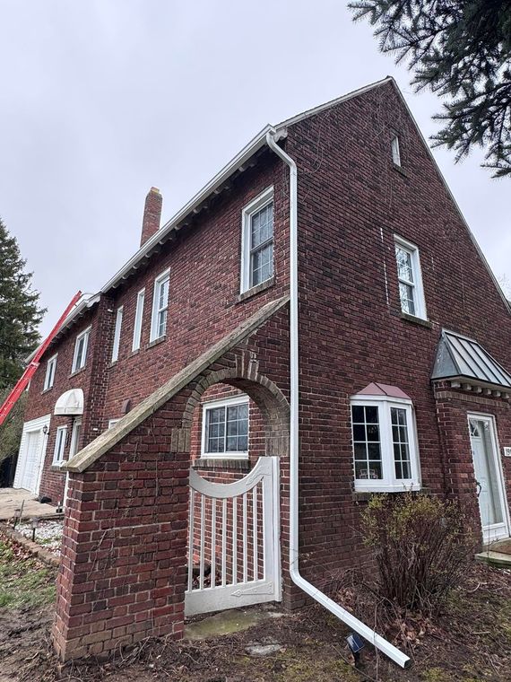 Red brick house with white trim and steep roof, viewed from a low angle on a cloudy day