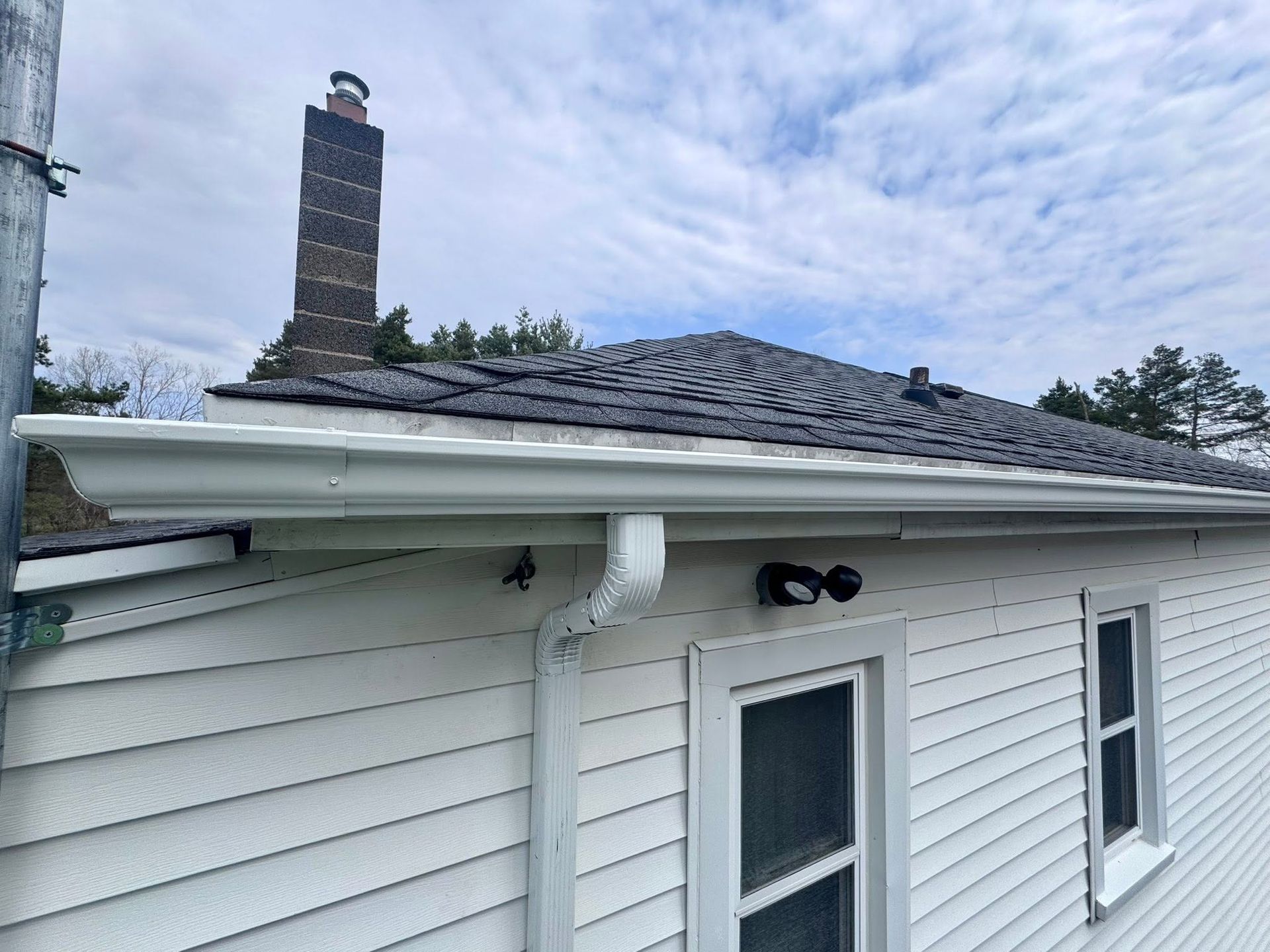 White-sided house with damaged shingle roof and a brick chimney under a cloudy sky