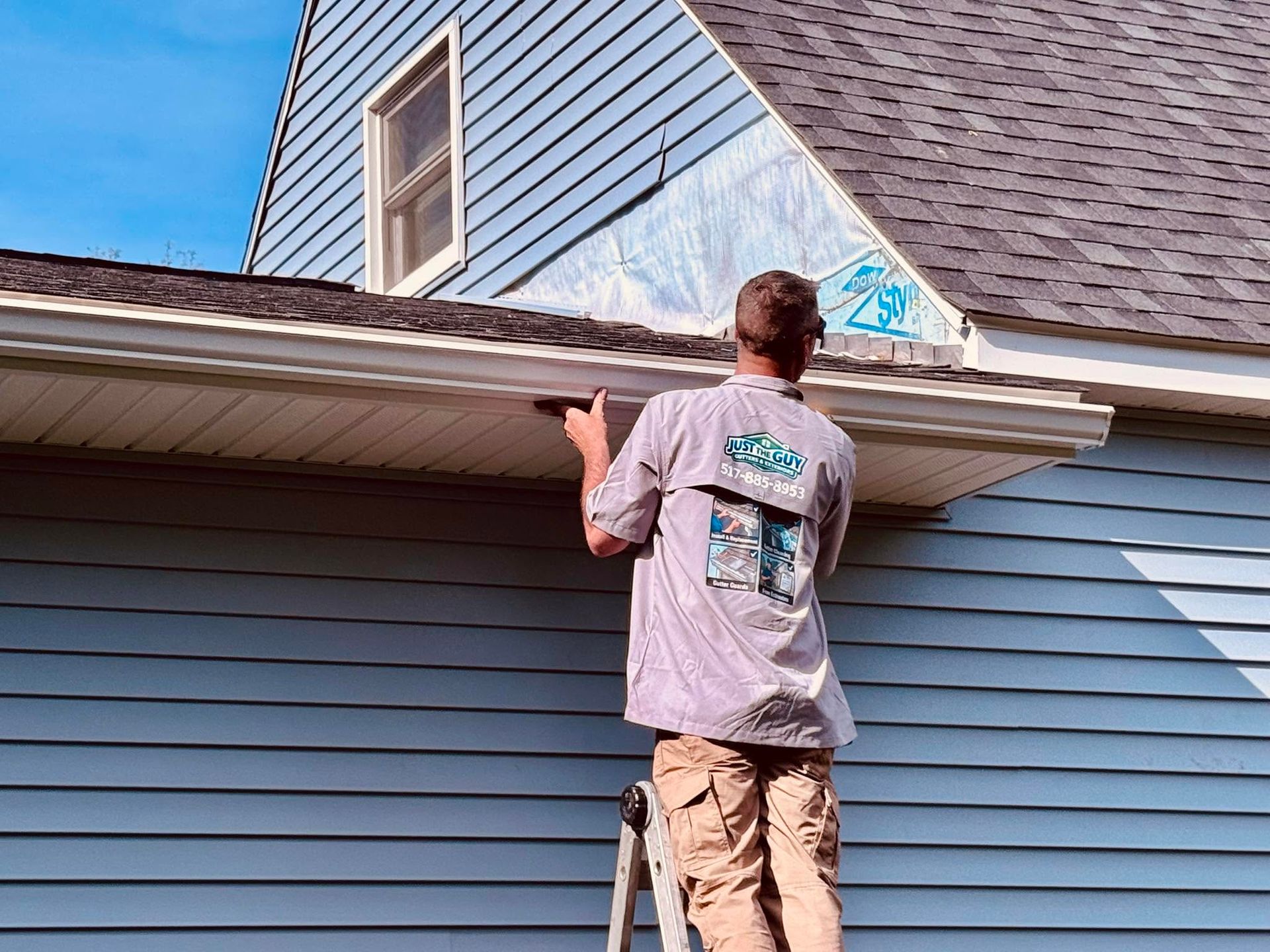 Worker on a ladder repairing the roof and siding of a house under blue sky