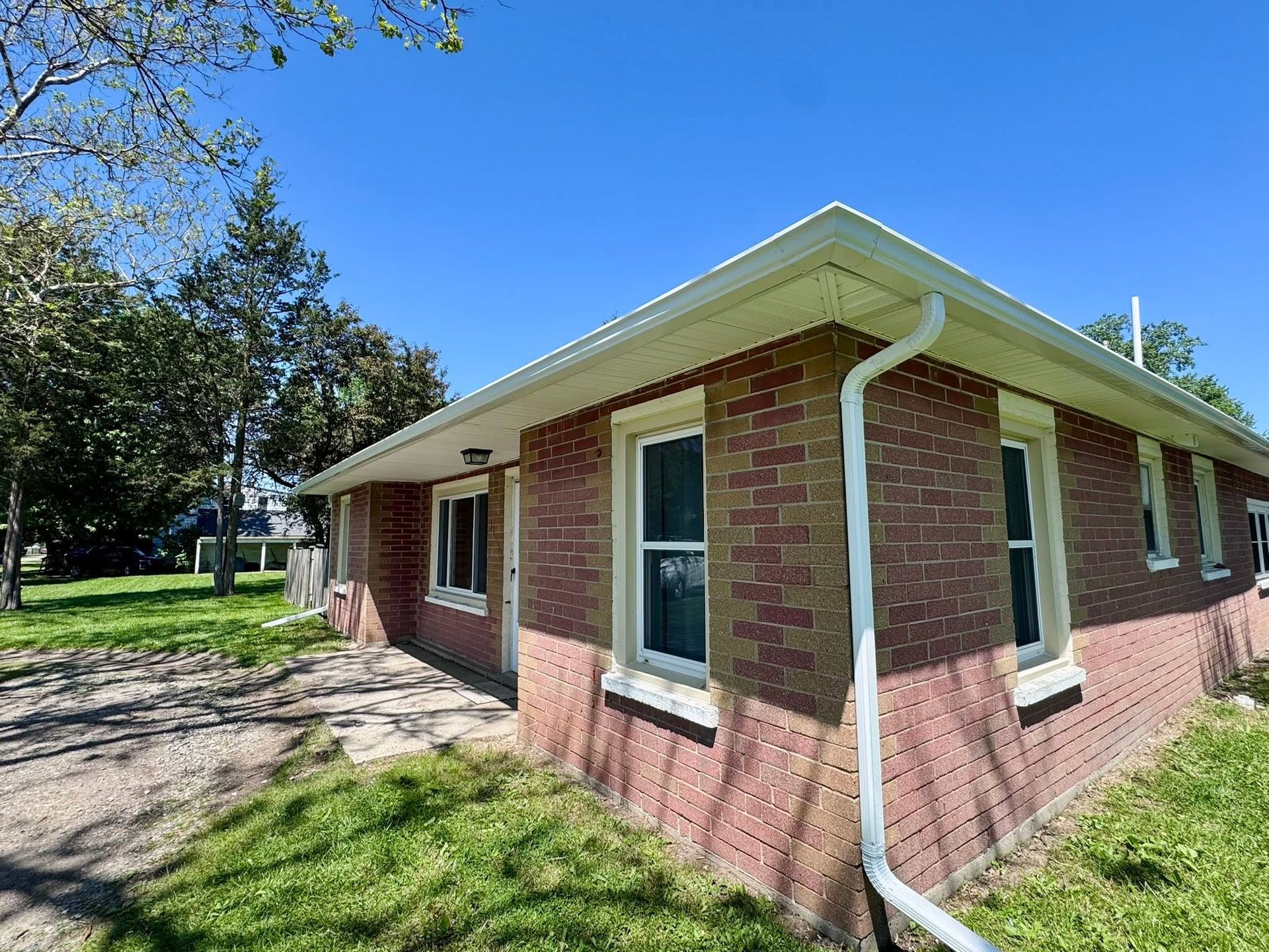 Brick house exterior with white trim and green shutters beside a grassy yard under a blue sky