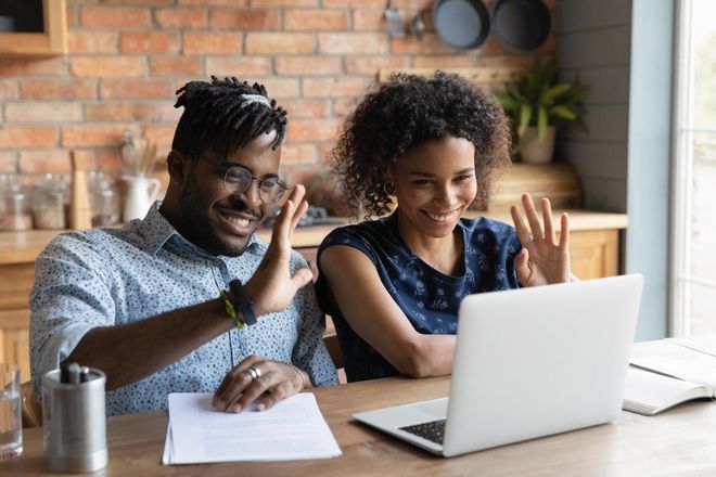 A man and a woman are sitting at a table looking at a laptop computer.